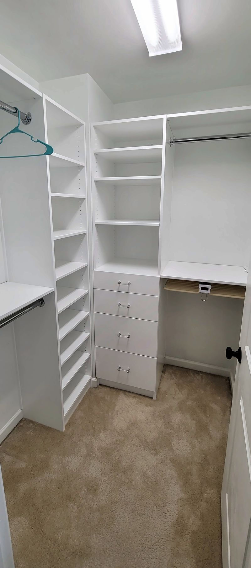 White walk-in closet system with adjustable shelves, a four-drawer bank, a shoe shelf tower and hanging rods
