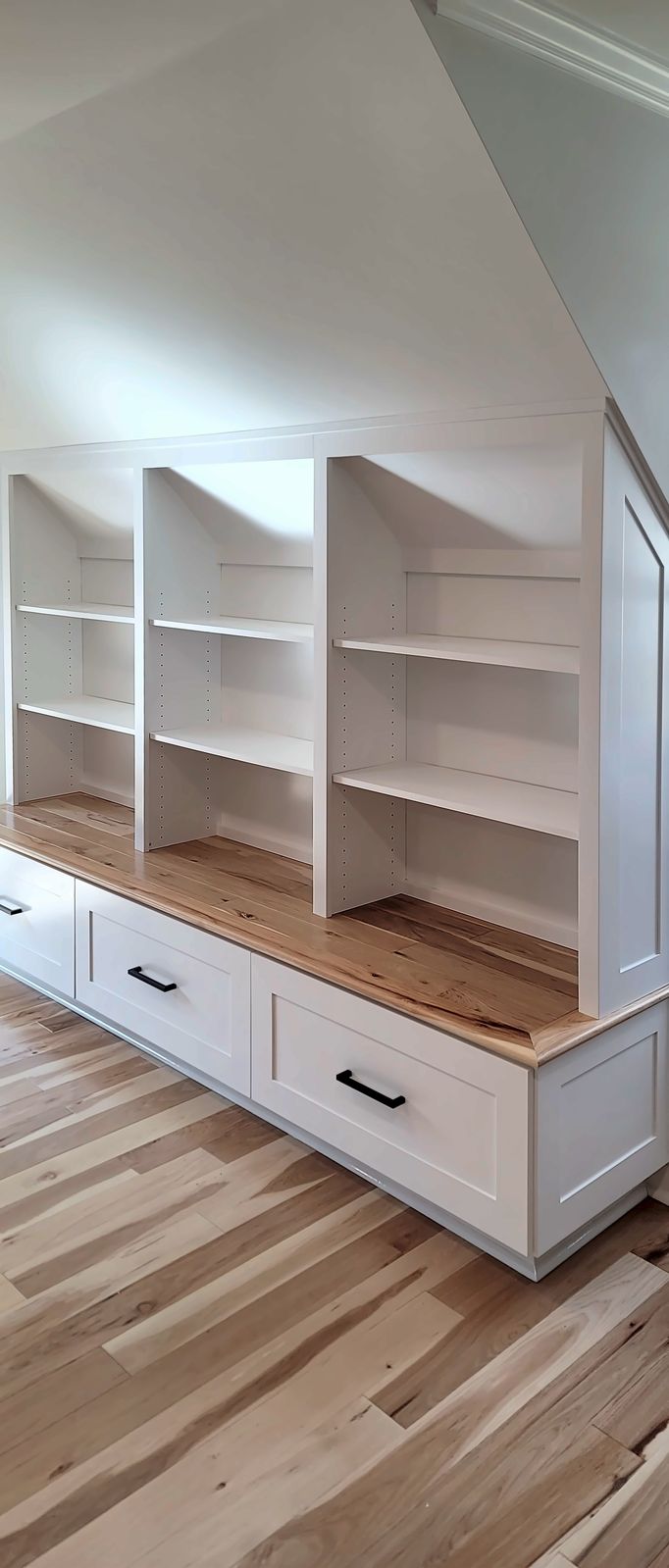 White built-in bookcases under a sloped ceiling with a butcher-block bench seat over a row of drawers
