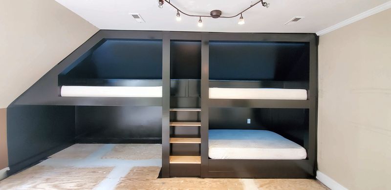 Black built-in bunk beds with four berths under a sloped ceiling and a ladder with open cubbies in the middle