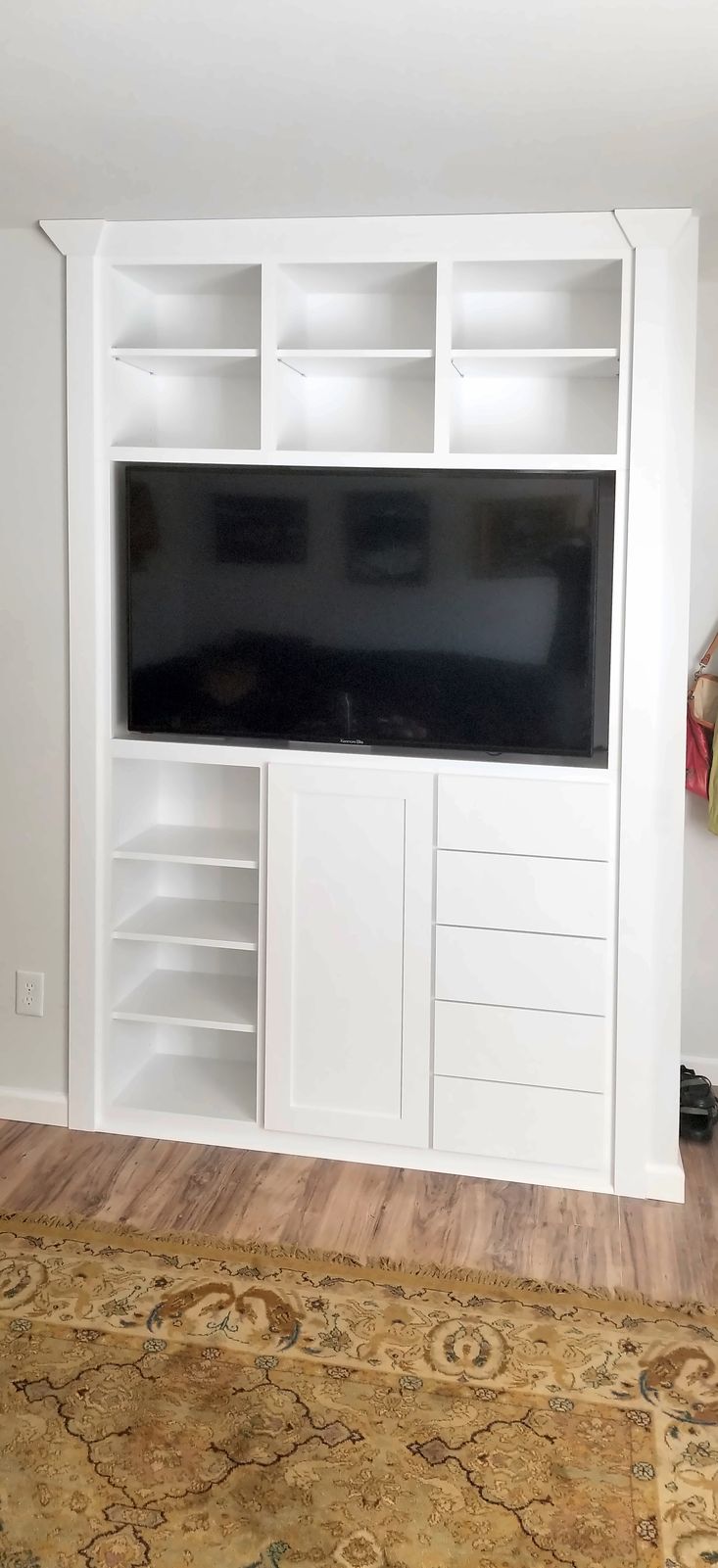 White built-in media cabinet with a television opening, open cubbies above and at the side, and drawers below