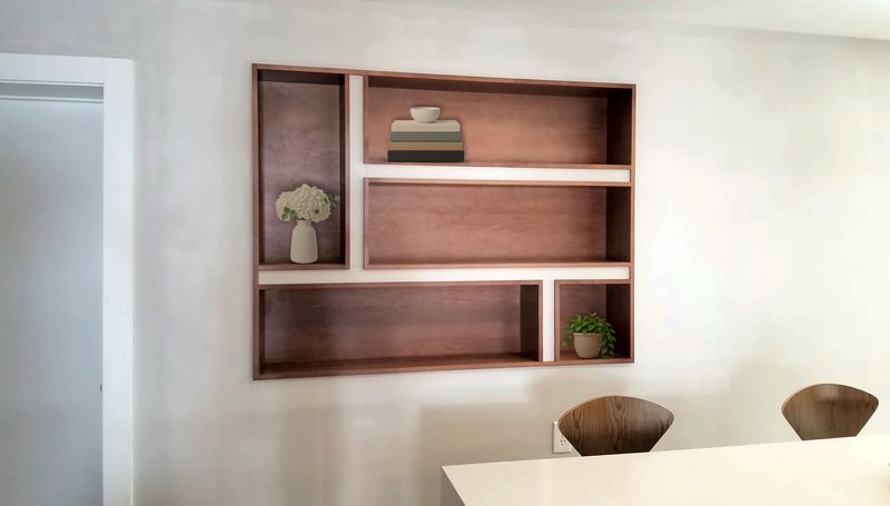 Walnut open-shelf unit with offset shelves and dividers set flush into a white wall niche, styled with books, a plant and a vase of flowers