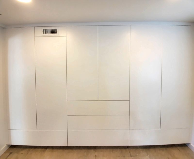 Wall of white flat-panel wardrobe cabinets from floor to ceiling, with a bank of drawers in the center section