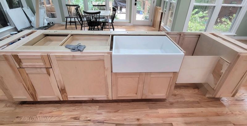 Natural wood kitchen island with a white farmhouse sink set in place, before the countertop is installed