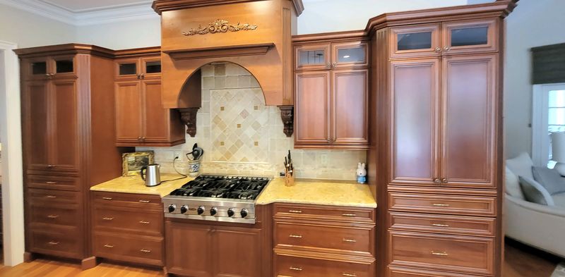 Traditional cherry kitchen with raised-panel doors, a wood range hood over a gas range, small glass-front upper cabinets and a tall pantry cabinet