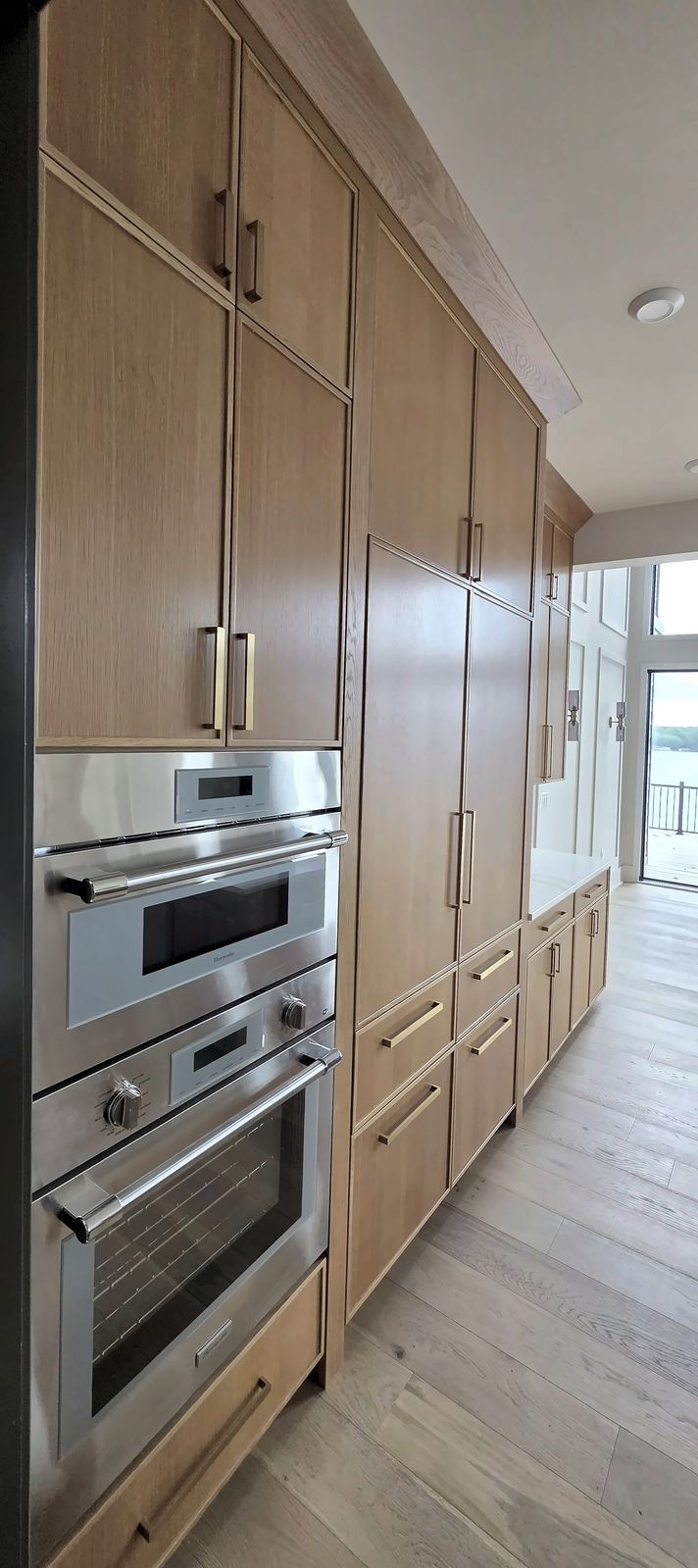 Tall light oak cabinet wall with two built-in wall ovens and long brass pulls, in a Macon, NC kitchen