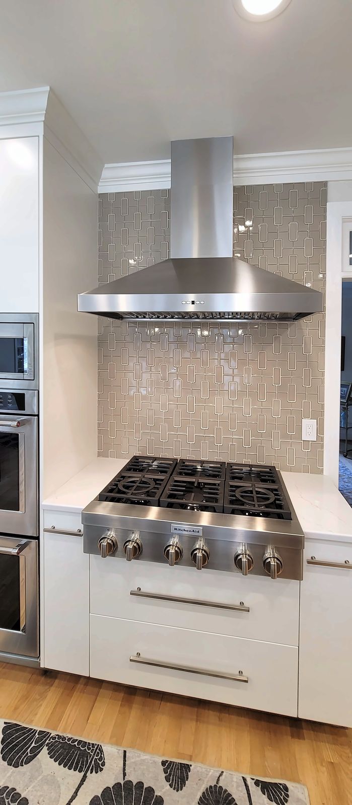 White shaker range wall with wide drawers under a gas cooktop, a stainless chimney hood and a tiled backsplash