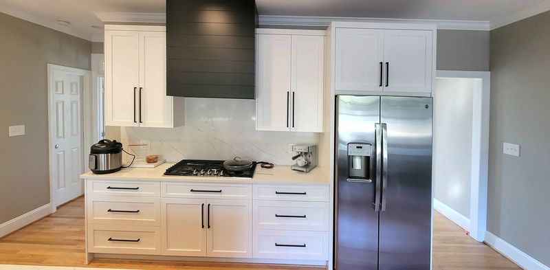 White shaker kitchen wall with drawer stacks, black bar pulls, a black shiplap range hood and a stainless refrigerator, with an espresso machine on the counter