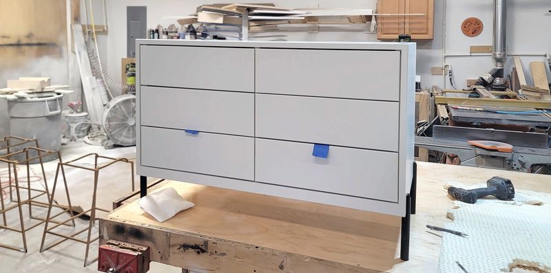 Light gray painted cabinet with six drawers standing on a bench in the shop