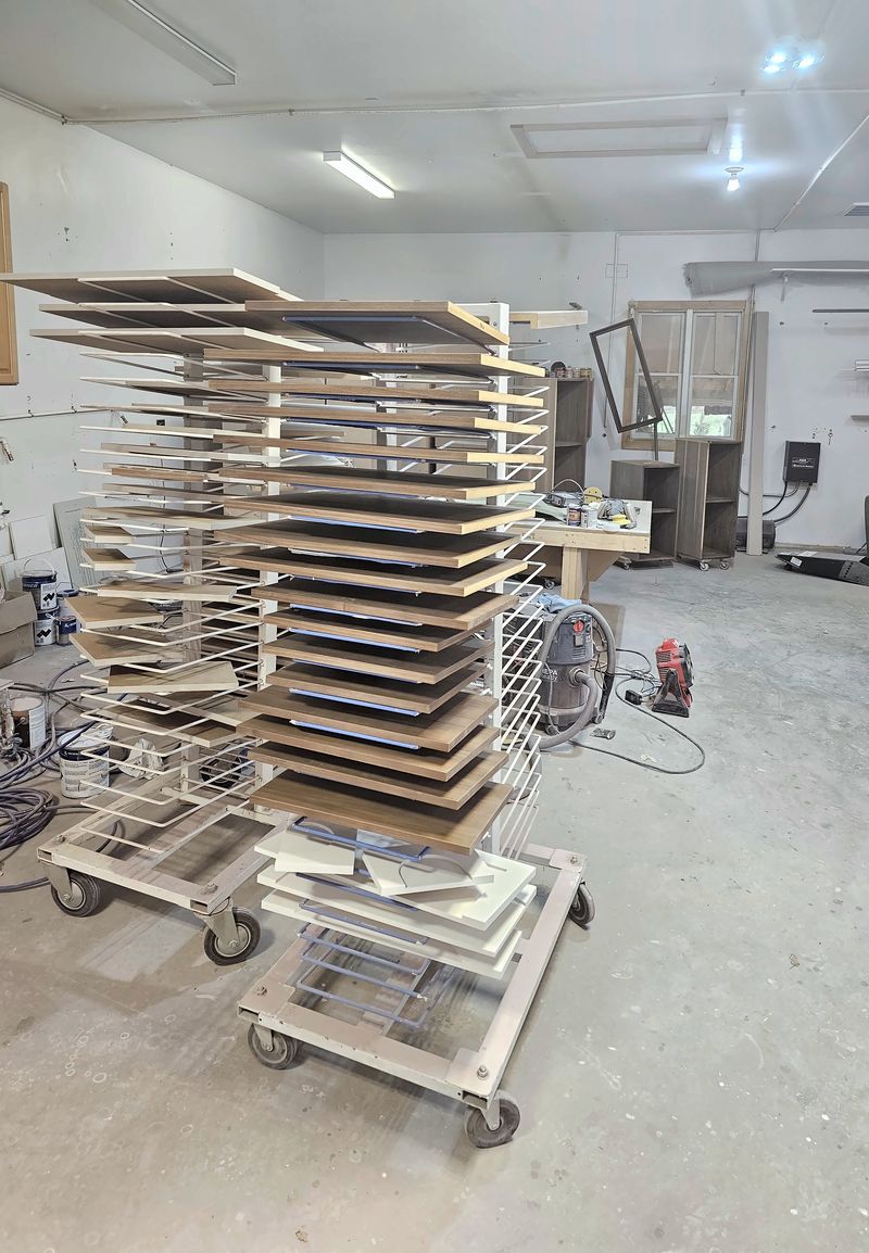 Rolling drying racks stacked with freshly finished cabinet doors and panels in the shop