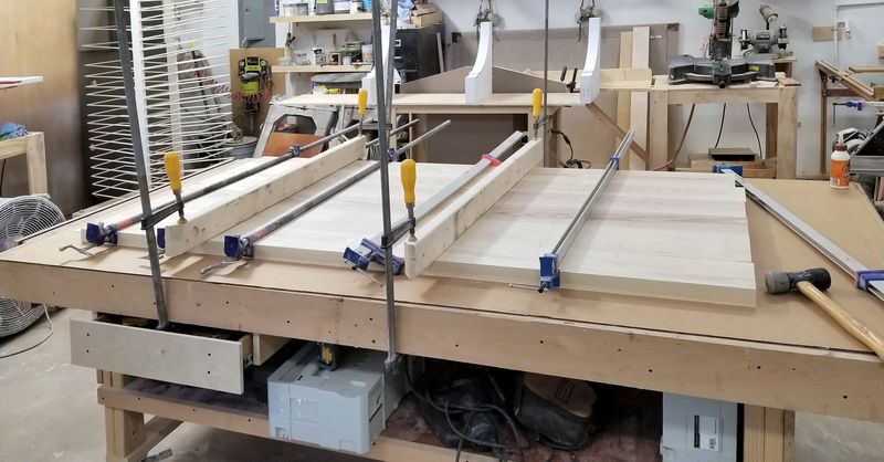Solid-wood panels held in long bar clamps on a workbench during glue-up