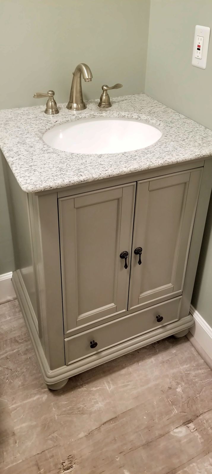 Gray painted single vanity with two raised-panel doors, turned feet and a speckled stone top with an undermount sink