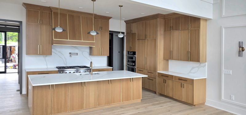 Custom kitchen in Macon, NC with light oak cabinetry, an oak range hood with brass inlay, a large island with a white quartz top, and brass pulls