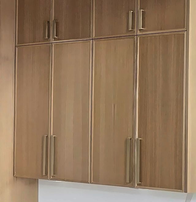 Light oak cabinet doors close up, showing pale, straight grain and long brass pulls